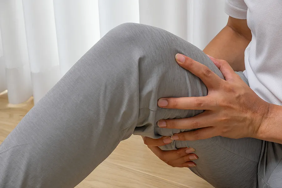 Person holding back of leg and lower thigh, representing hamstring strain or posterior leg pain